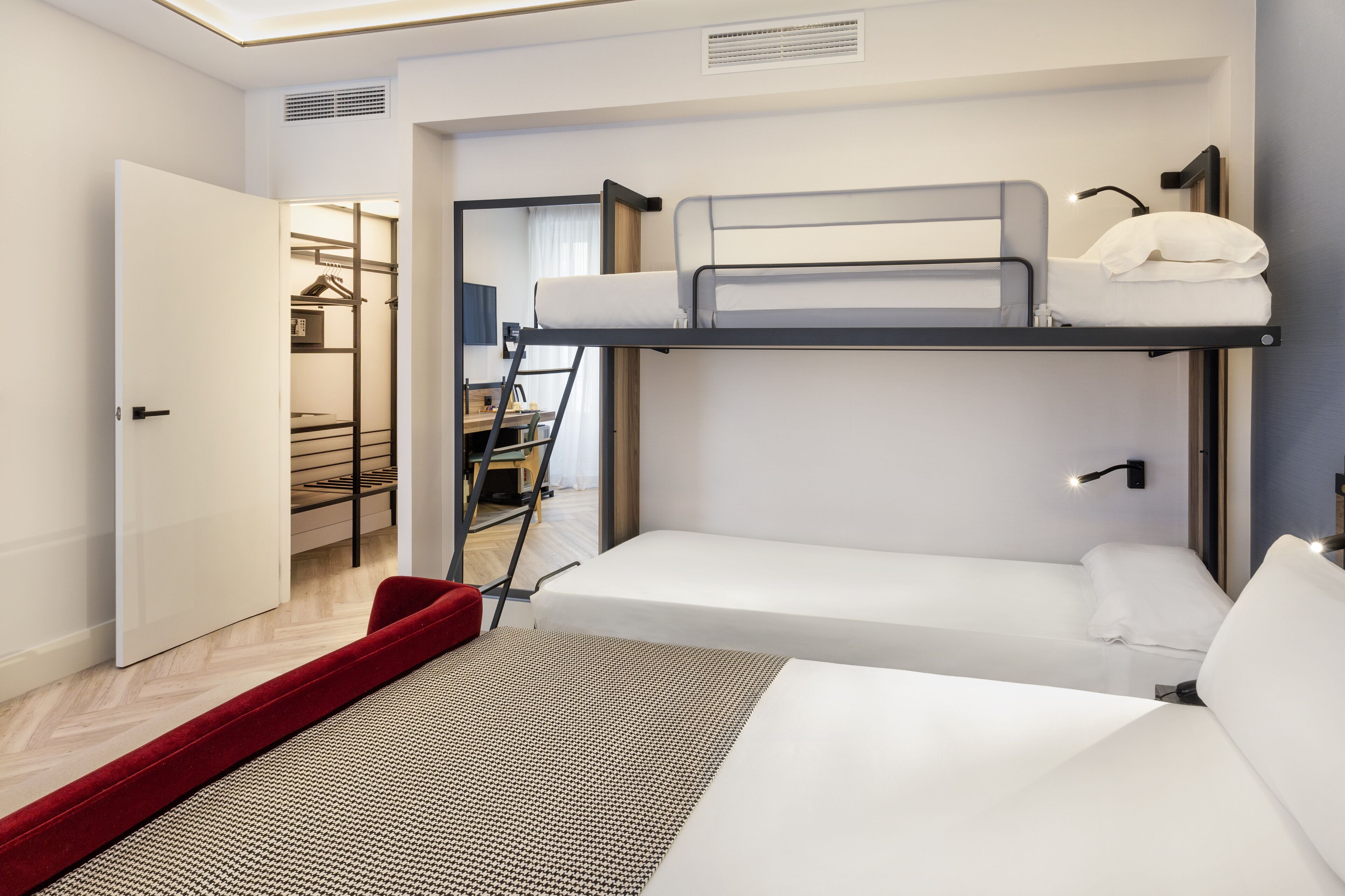 Habitación de hotel pequeña con literas, una cama individual, un armario y un escritorio con silla.