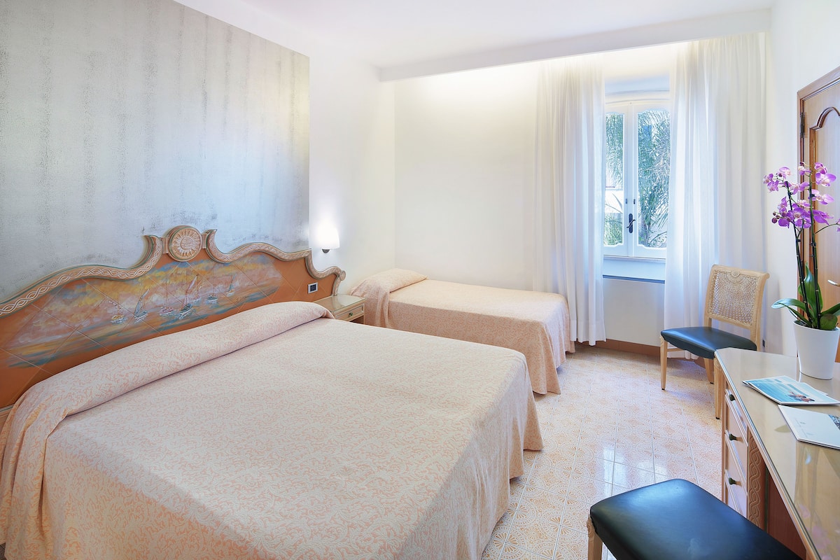 Habitación de hotel con dos camas, un escritorio, una silla y una ventana con cortinas.