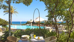 Ein Essbereich am Pool mit Korbstühlen, einem Tisch mit einer Schüssel Essen, Gläsern und einer Speisekarte.