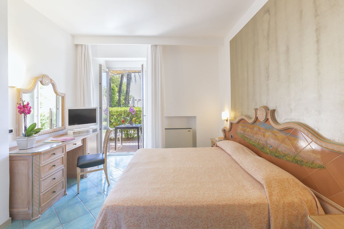Habitación de hotel con cama, escritorio con televisor, silla y pequeña mesa con planta.