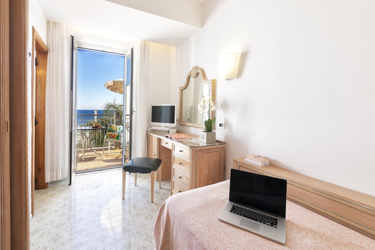 Habitación de hotel con cama, escritorio, laptop, televisión y vista al océano.