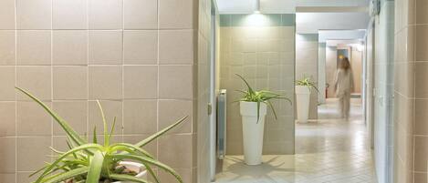 A corridor with tiled walls, potted plants, and a person walking in the distance.