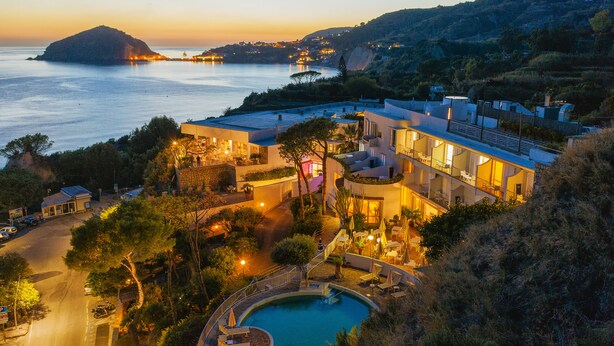 Un hotel frente al mar con piscina, mobiliario exterior y vistas al océano.