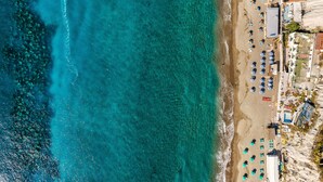Vista aérea de una playa con aguas turquesas cristalinas, una fila de sombrillas y un edificio con techo rojo.