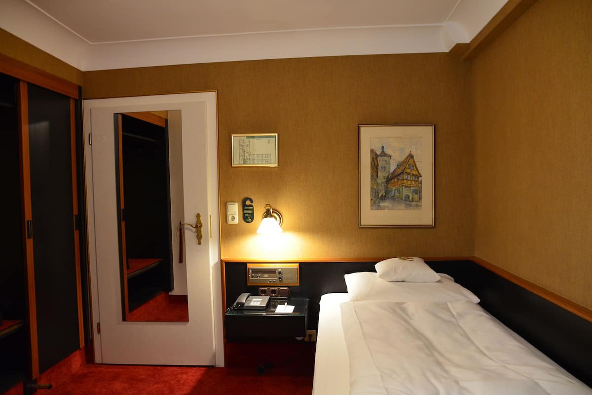 Habitación de hotel con cama, mesita de noche con lámpara, teléfono y un cuadro en la pared.