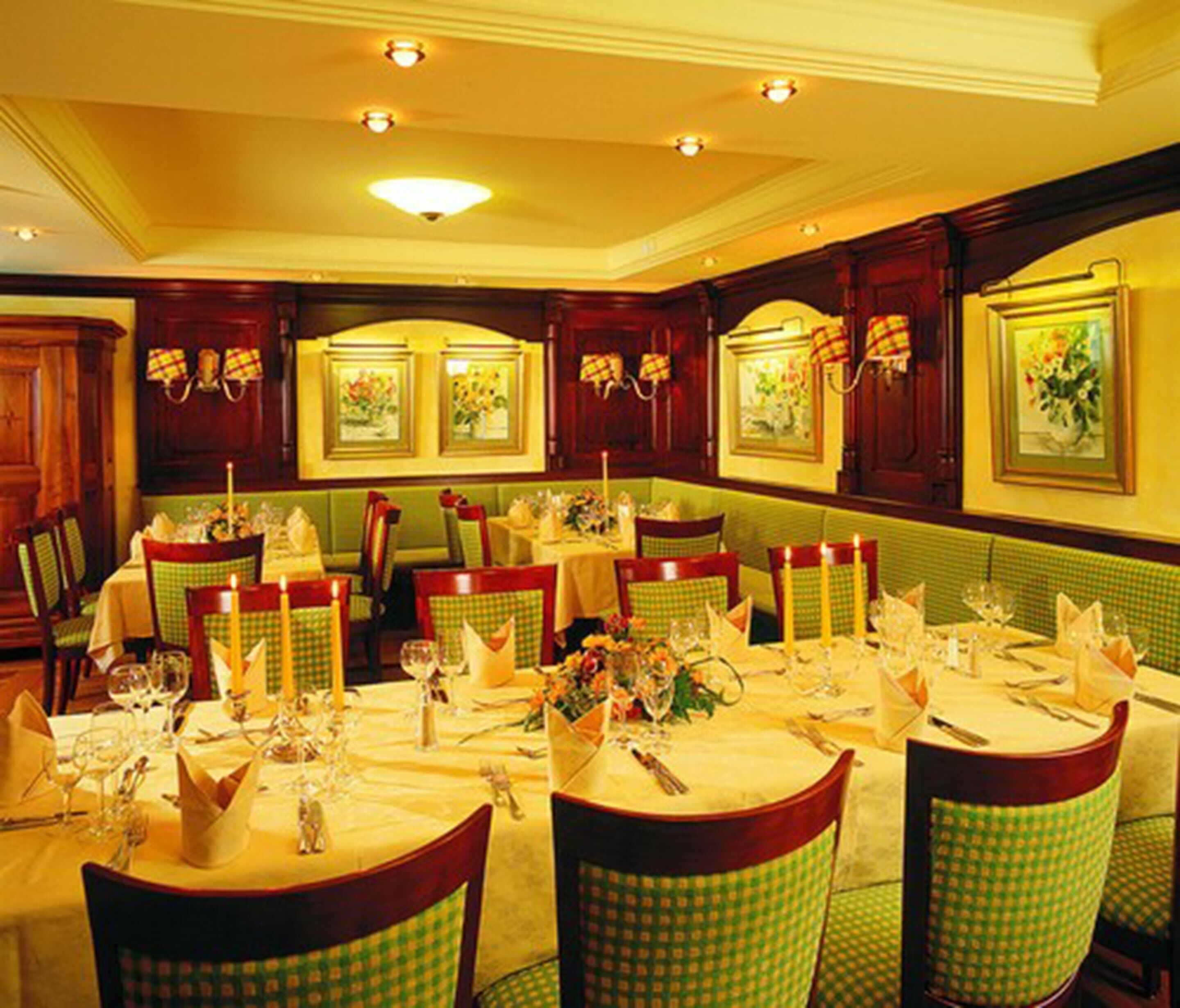 A formal dining room with multiple tables set for service, featuring checkered tablecloths and green upholstered chairs.