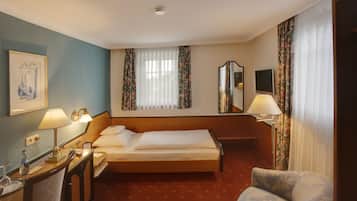 Habitación de hotel con cama, escritorio con lámpara, silla, televisión y ventana con cortinas.