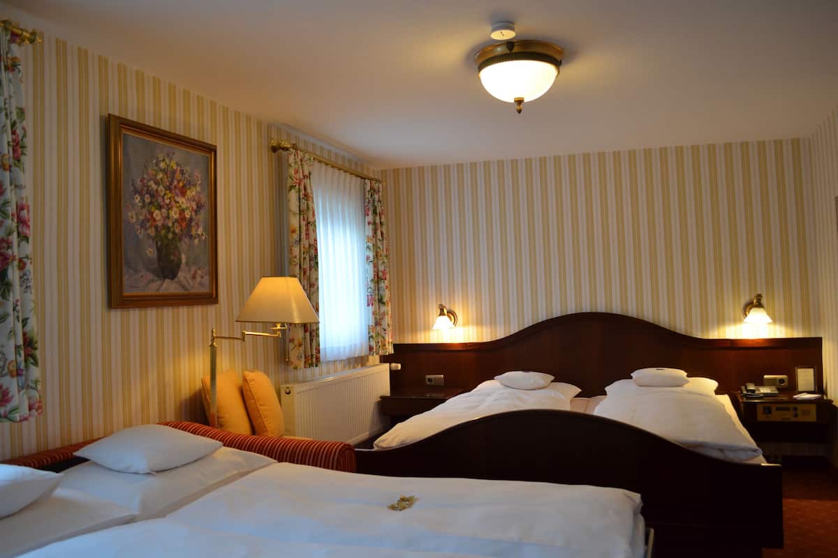 Habitación de hotel con dos camas, papel tapiz a rayas, cortinas florales, un cuadro y lámparas de noche.
