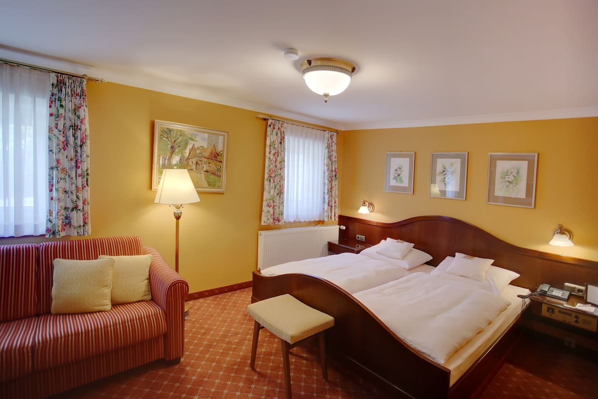 Habitación de hotel con cama doble, sofá a rayas, una mesita y una ventana con cortinas.