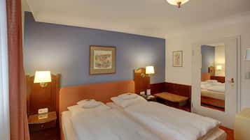 Habitación de hotel con dos camas, una mesita de noche con lámpara, una pequeña mesa y un espejo en la pared.