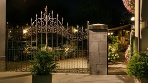 Una reja de hierro forjado con diseños intrincados y un adorno de estrella, que da acceso a un edificio con un pilar de piedra y plantas en macetas.