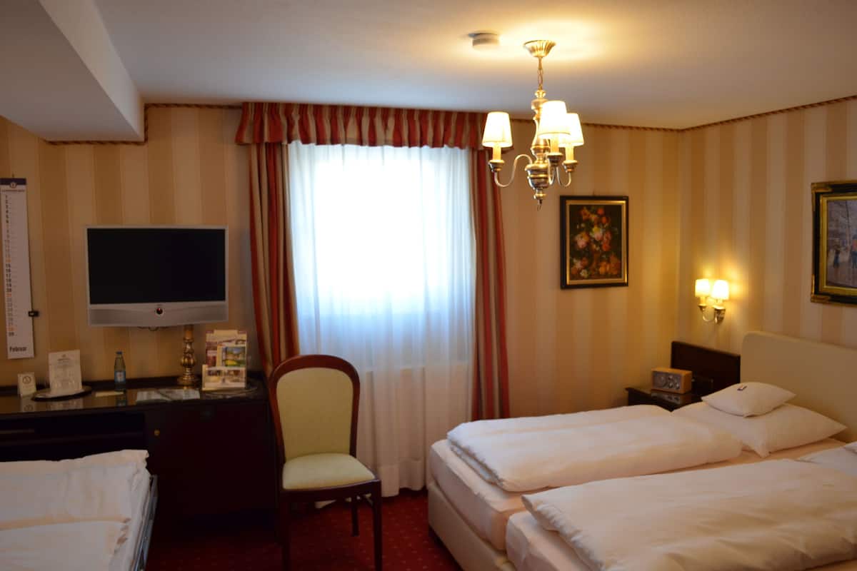 Habitación de hotel con dos camas, un escritorio con televisor, una silla, una lámpara de escritorio y un cuadro en la pared.