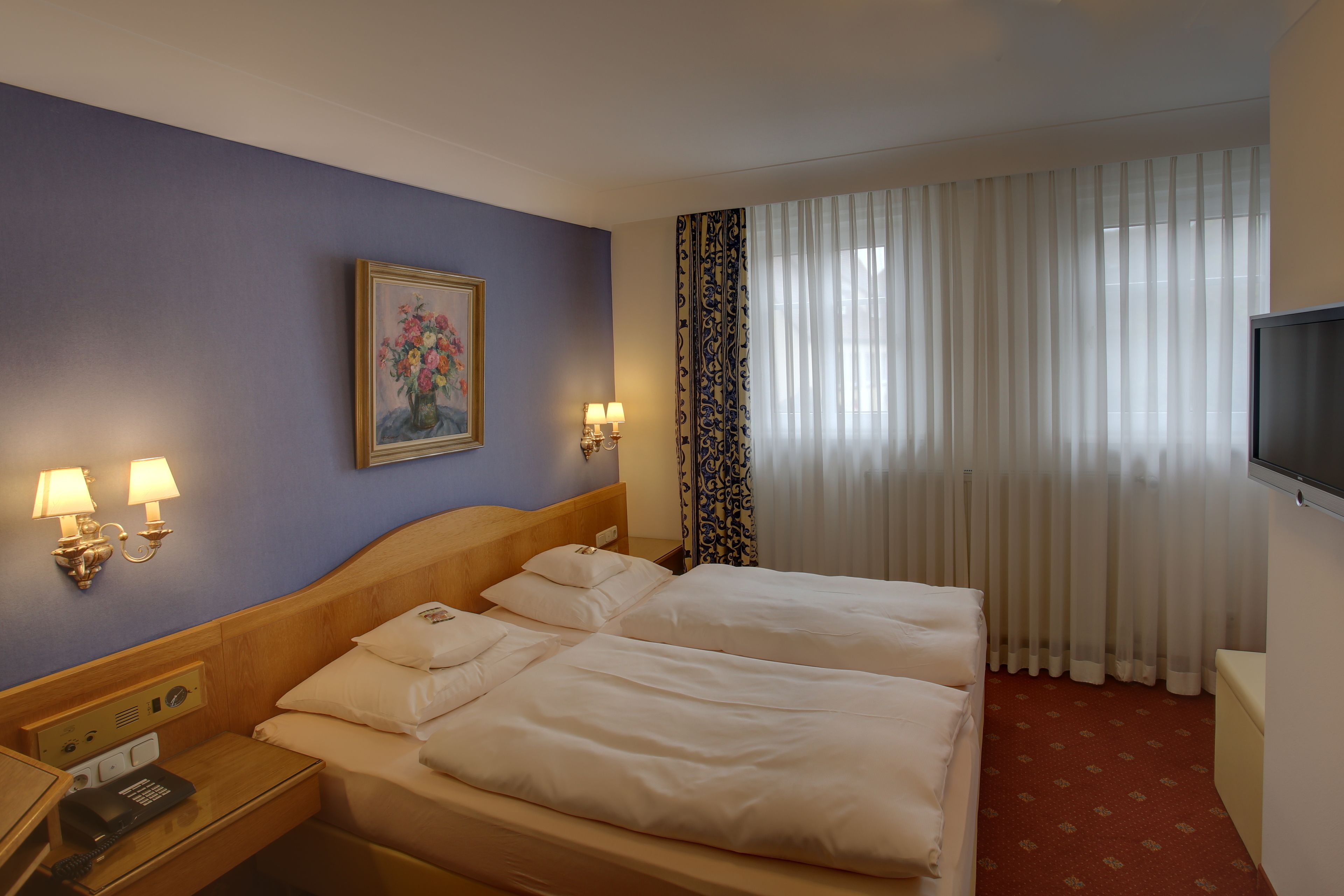 A hotel room with two beds, a painting on the wall, a TV, and a telephone on the nightstand.