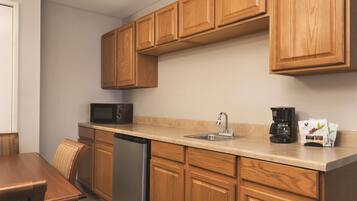 A compact kitchen with wooden cabinets, a dishwasher, a microwave, a sink with a faucet, and a coffee maker.