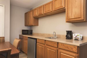 Una cocina compacta con armarios de madera, lavavajillas, microondas, pileta con grifo y cafetera.