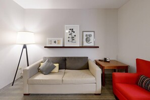 Une pièce avec un canapé blanc, un divan rouge, une lampe, une petite table et des œuvres d’art encadrées accrochées au mur.