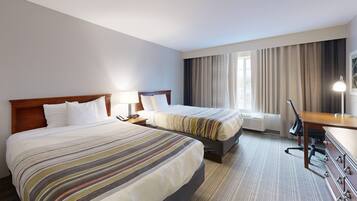 A hotel room with two beds, a desk, a chair, a lamp, and a window with curtains.