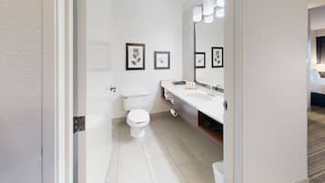 Un baño moderno con inodoro, lavamanos y espejo. Se observan cuadros enmarcados en la pared.