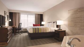 A hotel room with a bed, a desk, a chair, a TV, a lamp, a bathroom with a sink and a bathtub.