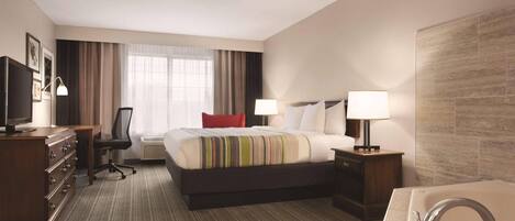 A hotel room with a bed, a desk, a chair, a TV, a lamp, a bathroom with a sink and a bathtub.