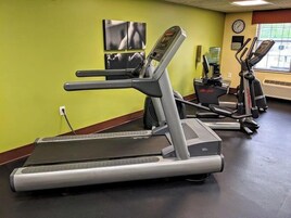 Un gimnasio con cintas de correr, un reloj de pared y un dispensador de agua.