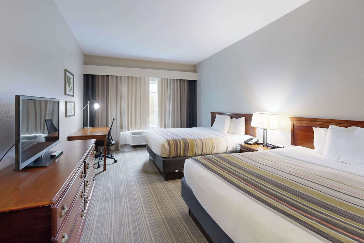 Une chambre d’hôtel avec deux lits, un bureau avec un ordinateur, une télévision et une fenêtre avec des rideaux.