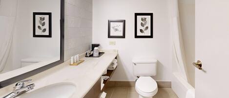 A bathroom with a sink, toilet, and shower. There are framed pictures on the wall.