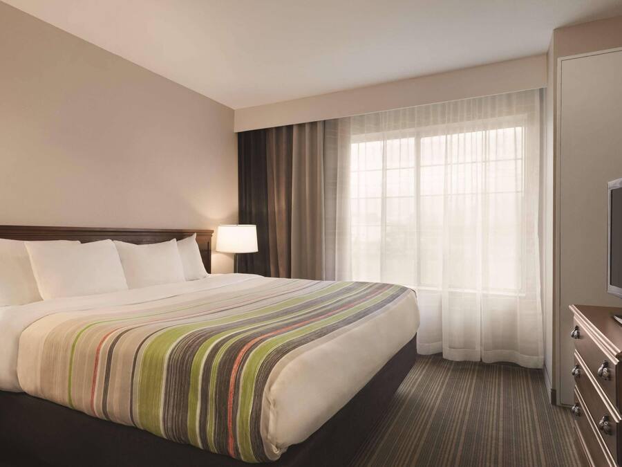 A hotel room with a large bed, a television, a desk, and a window with curtains.