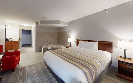 A hotel room with a large bed, a bathroom with a bathtub, a desk with a chair, and a small table with a lamp.