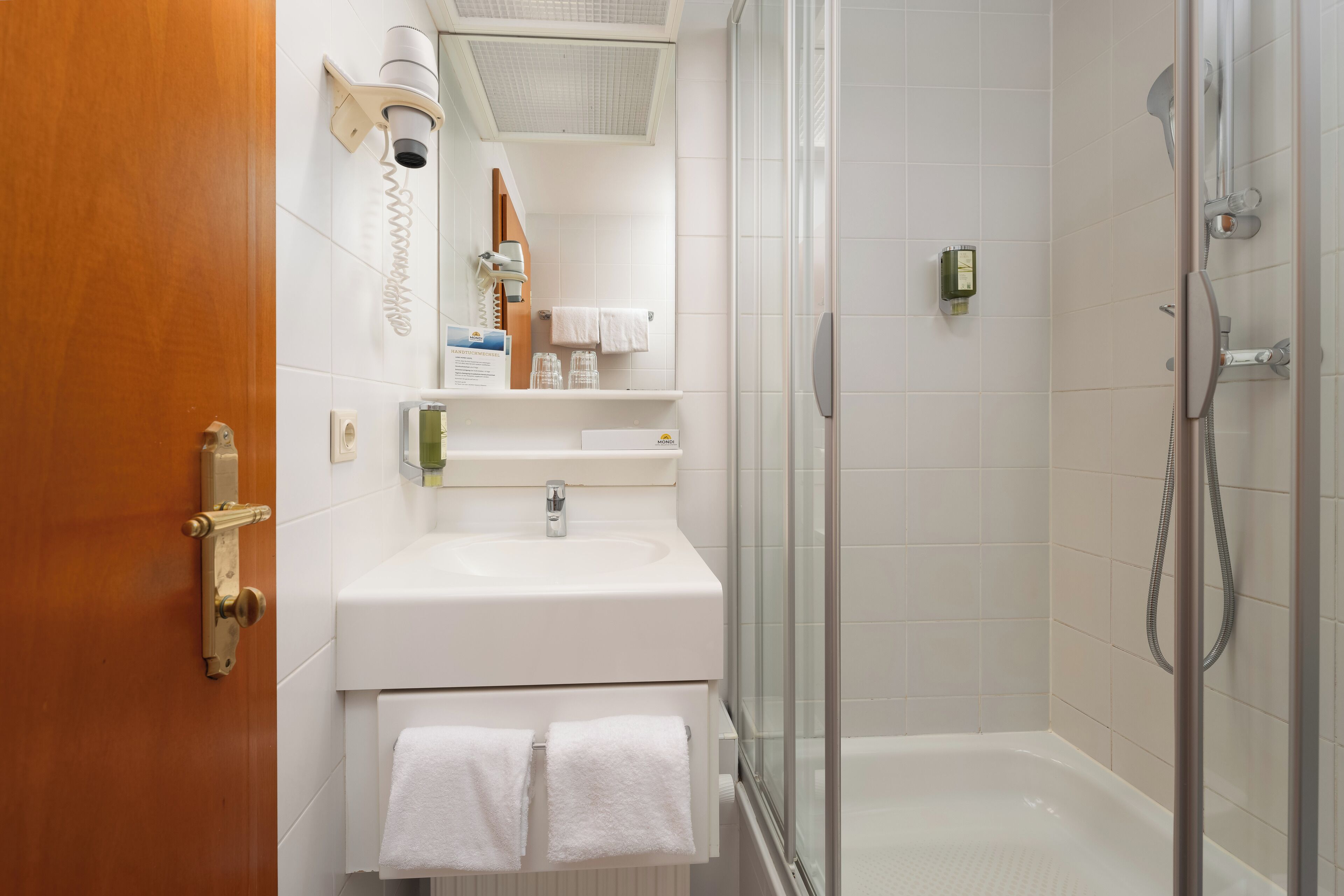 Een moderne badkamer met een witte wastafel, een glazen douchecabine en een houten deur.