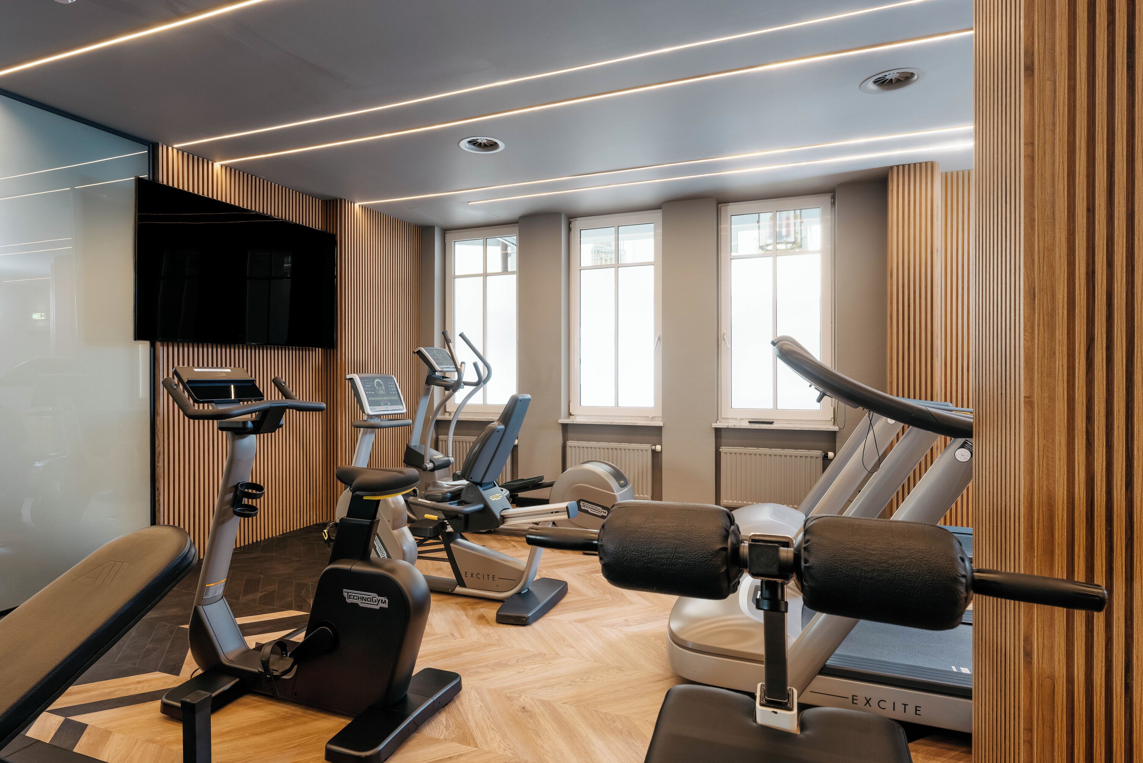 Een moderne sportschool met diverse fitnessapparaten, grote ramen en een wandbekleding van hout.