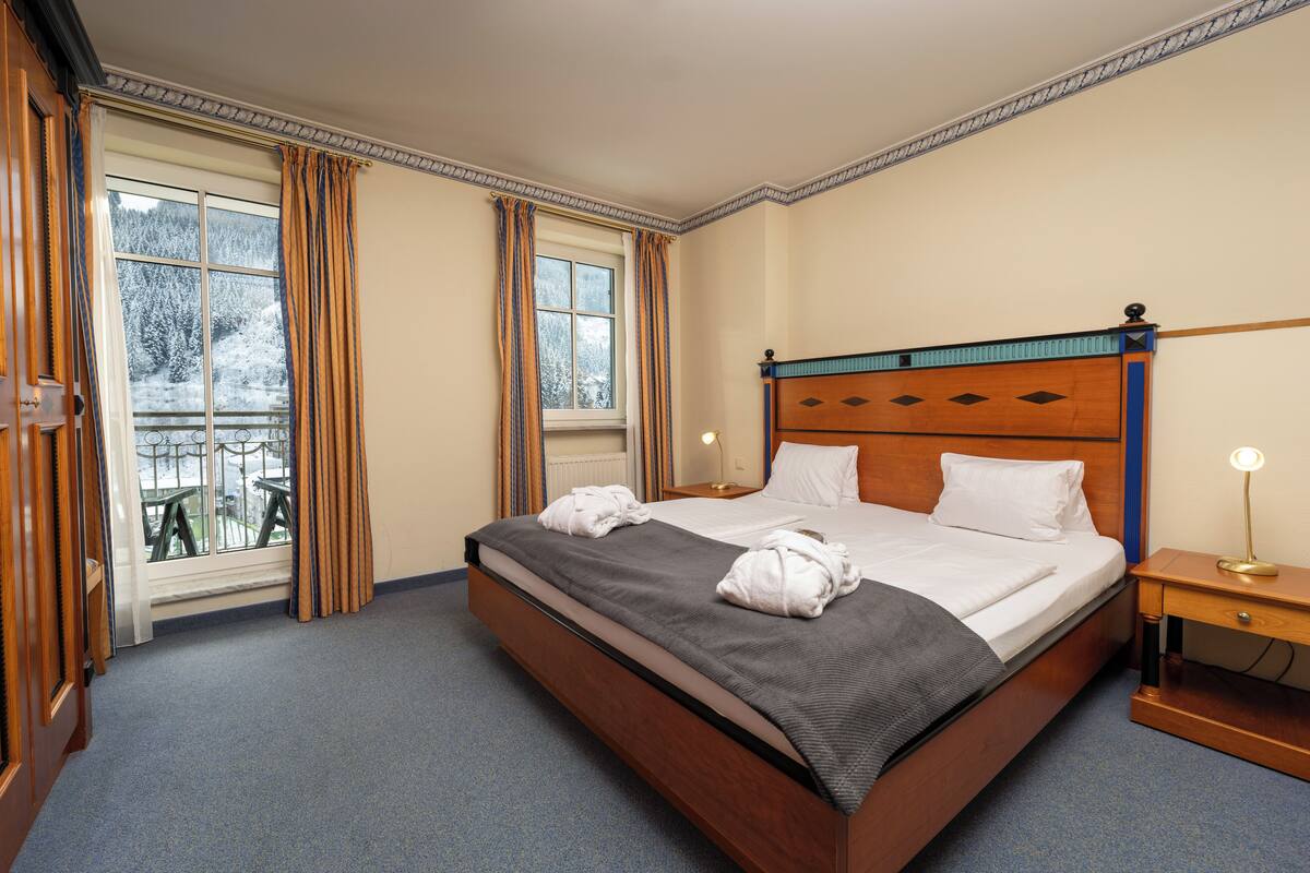 Une chambre d’hôtel avec un grand lit, une table de chevet, une lampe et une fenêtre avec des rideaux.