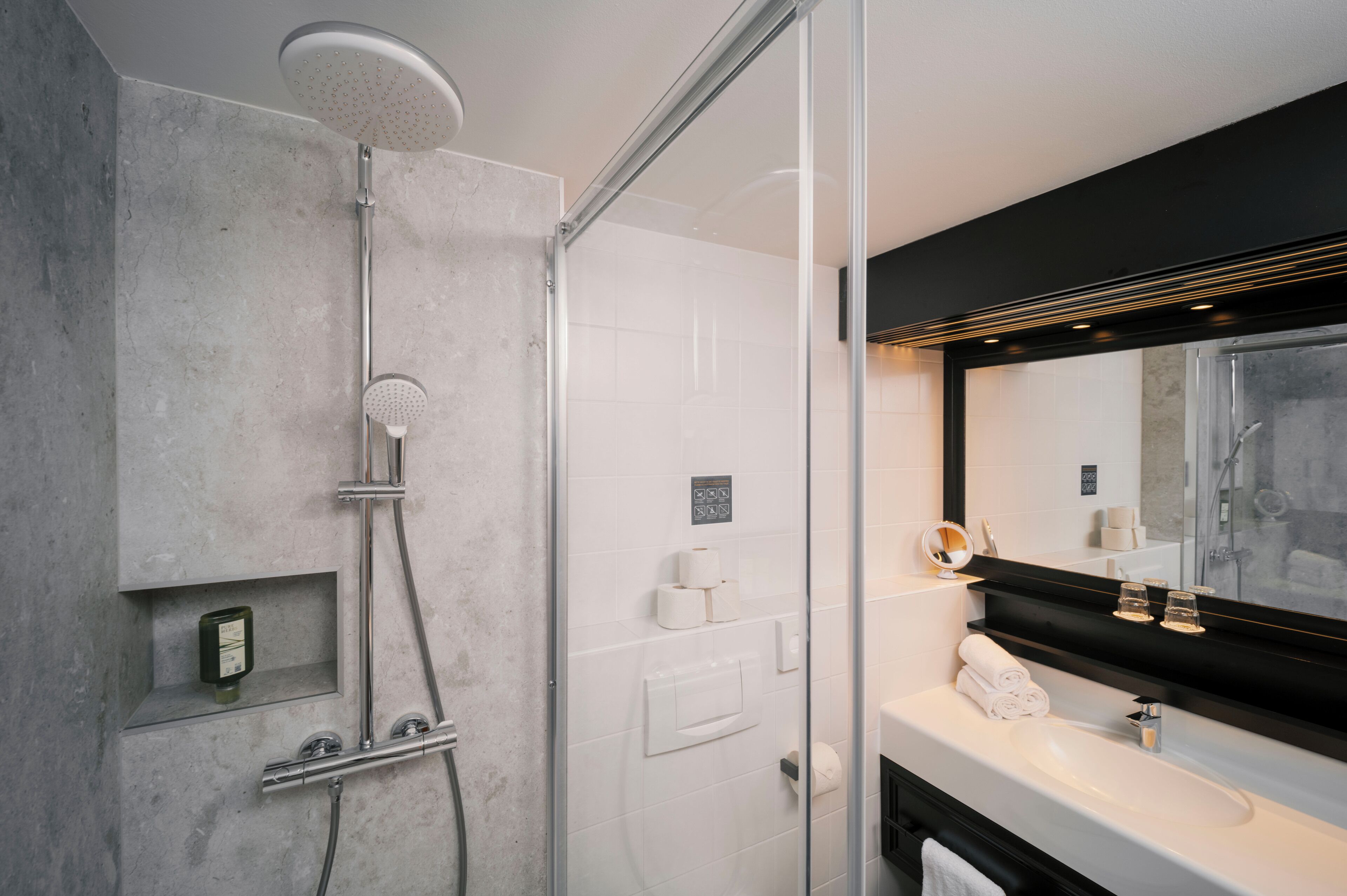 A modern bathroom with a glass-enclosed shower, a large mirror, and a white sink.