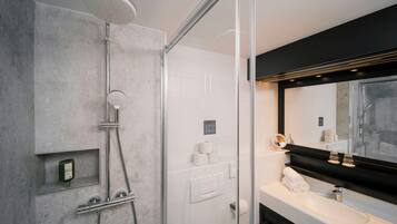 A modern bathroom with a glass-enclosed shower, a large mirror, and a white sink.