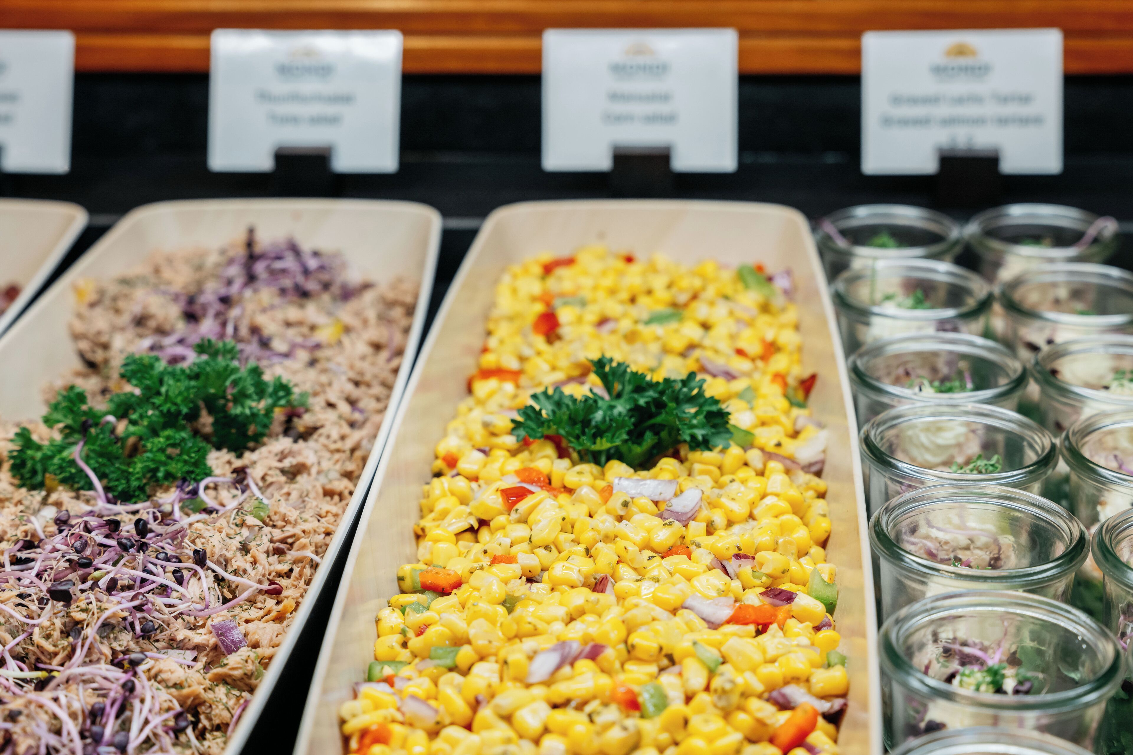 A buffet with various dishes including shredded meat, corn salad, and mixed greens in glass containers.