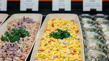 A buffet with various dishes including shredded meat, corn salad, and mixed greens in glass containers.