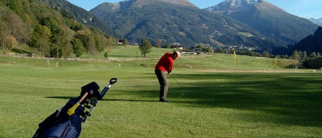 A golf course with a golf bag and a golfer in a red shirt.