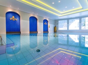 A spacious indoor swimming pool with clear blue water, surrounded by walls with blue mosaic tiles and gold decorative elements. - MONDI Hotel Bellevue Gastein (Bad Gastein)
