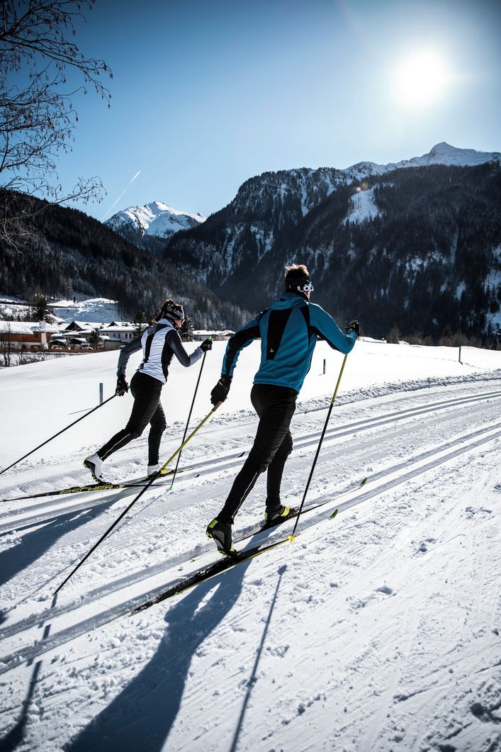 Deux skieurs sur une piste enneigée, avec des montagnes en arrière-plan.