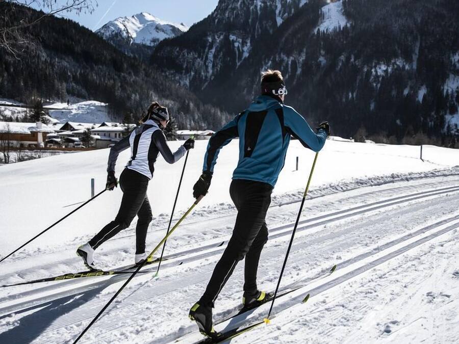 Deux skieurs sur une piste enneigée, avec des montagnes en arrière-plan.