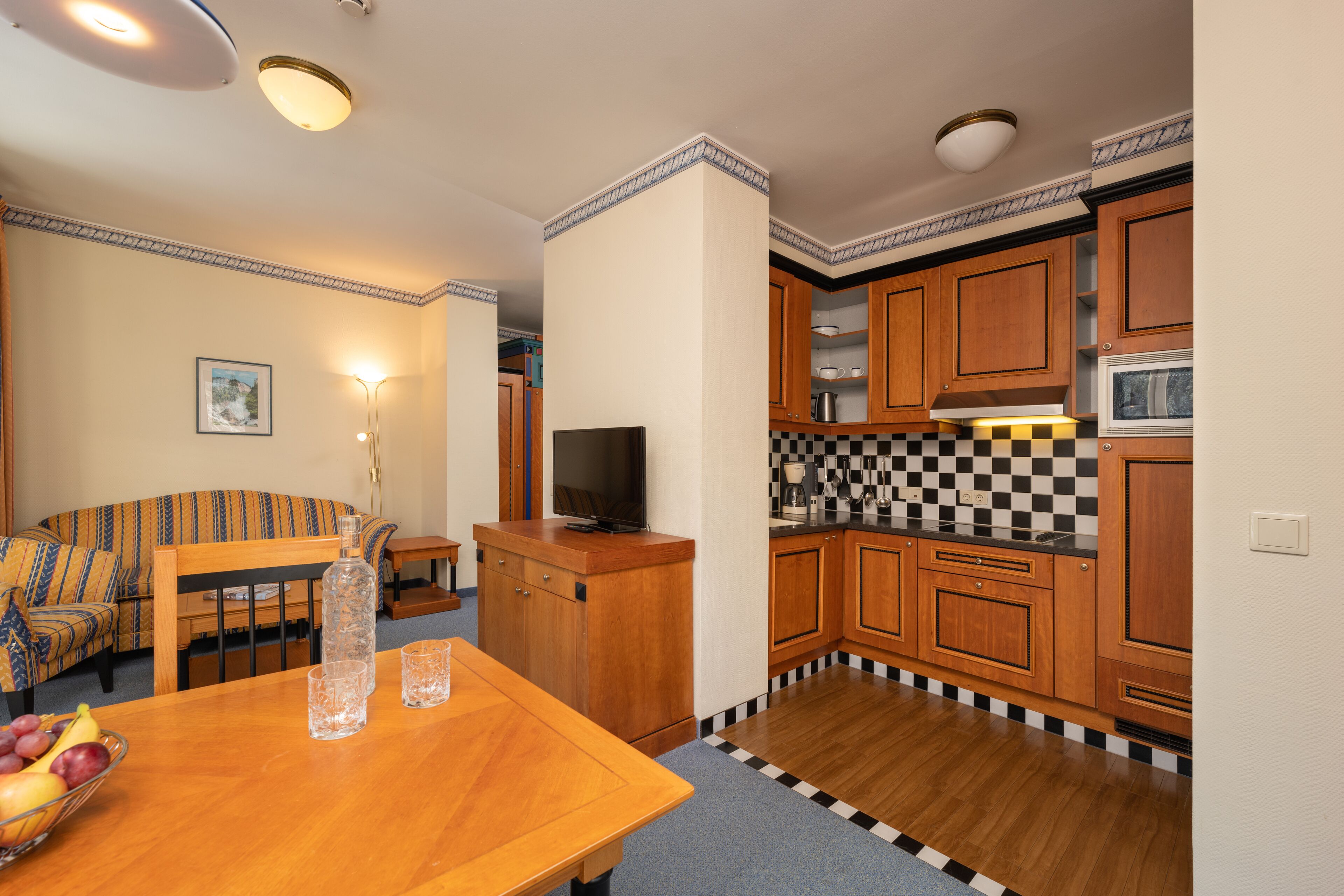 Una cocina compacta con armarios de madera, salpicadero a cuadros y una zona de comedor con una mesa y sillas.