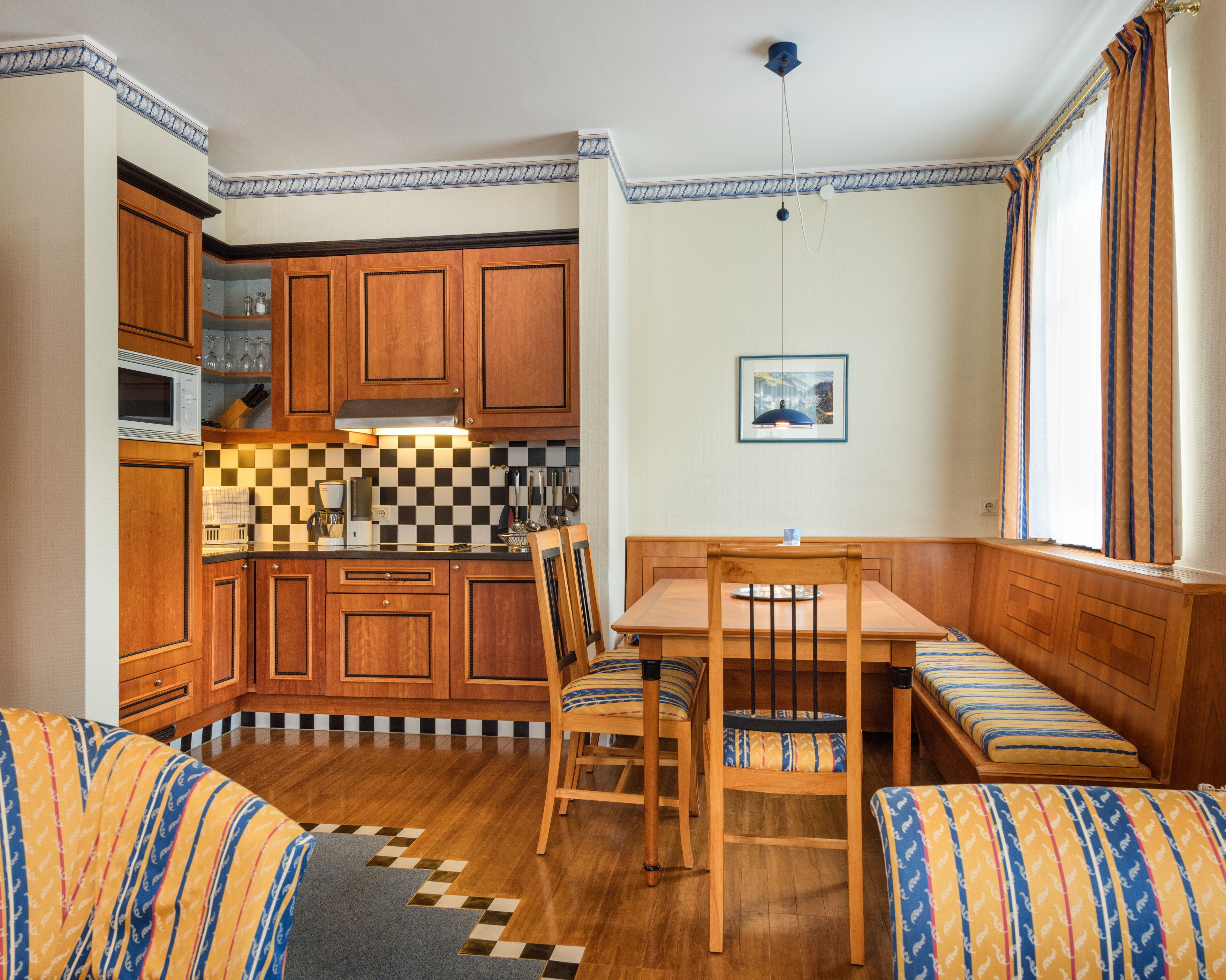 Una cocina compacta con armarios de madera, un microondas y un salpicadero de cuadros. Hay una mesa de comedor con sillas y un banco.
