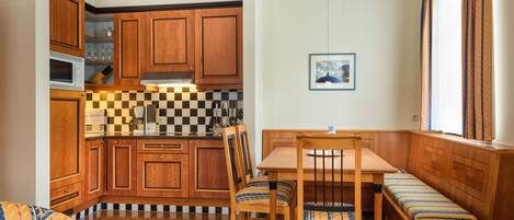 Una cocina compacta con armarios de madera, un microondas y un salpicadero de cuadros. Hay una mesa de comedor con sillas y un banco.