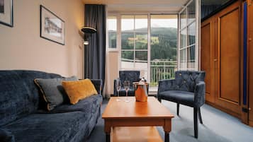 A room with a sofa, two armchairs, a wooden table, and a large window with a view of a mountain landscape.