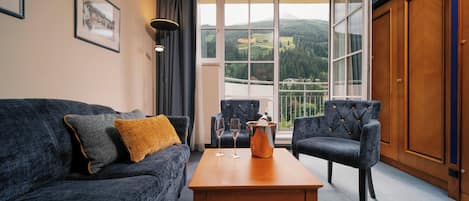 A room with a sofa, two armchairs, a wooden table, and a large window with a view of a mountain landscape.