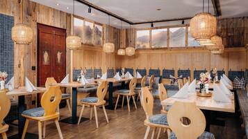 A restaurant with wooden walls, large windows, and hanging wicker lamps. Tables are set with white napkins and centerpieces.