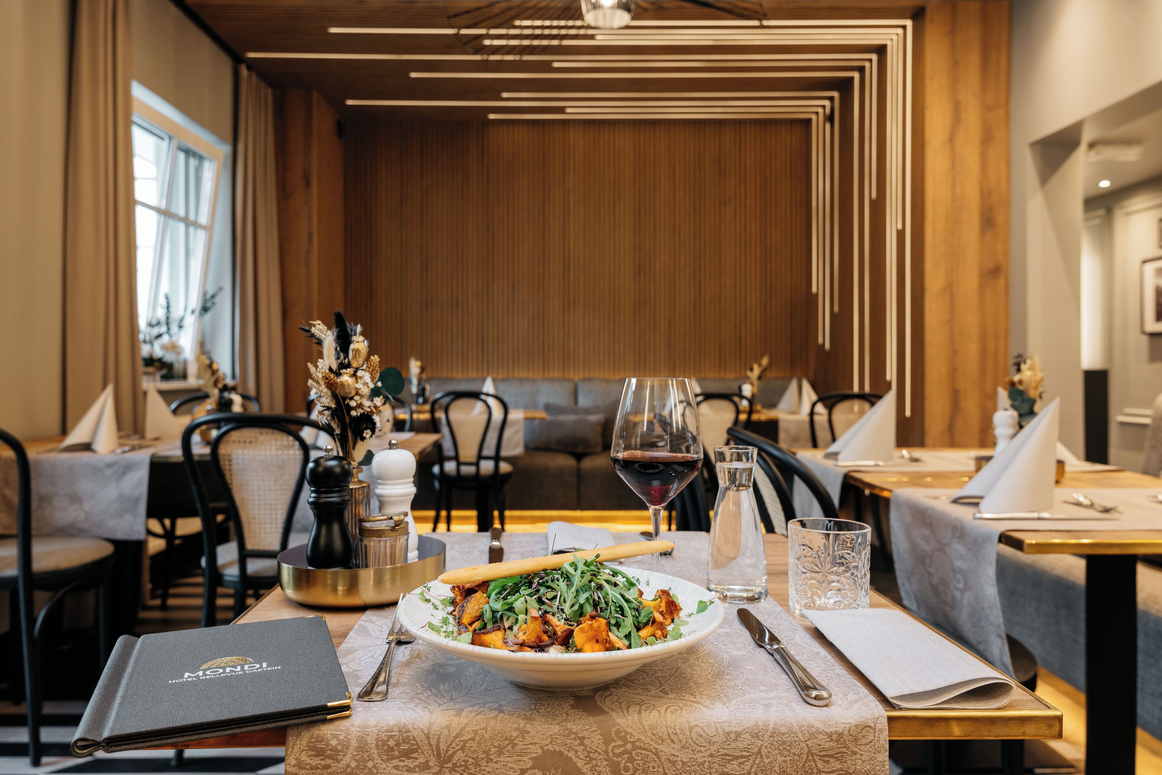 Ein Restaurant mit Holzinneneinrichtung, ein Tisch gedeckt mit einem Teller Essen, Weingläsern und einer Speisekarte.