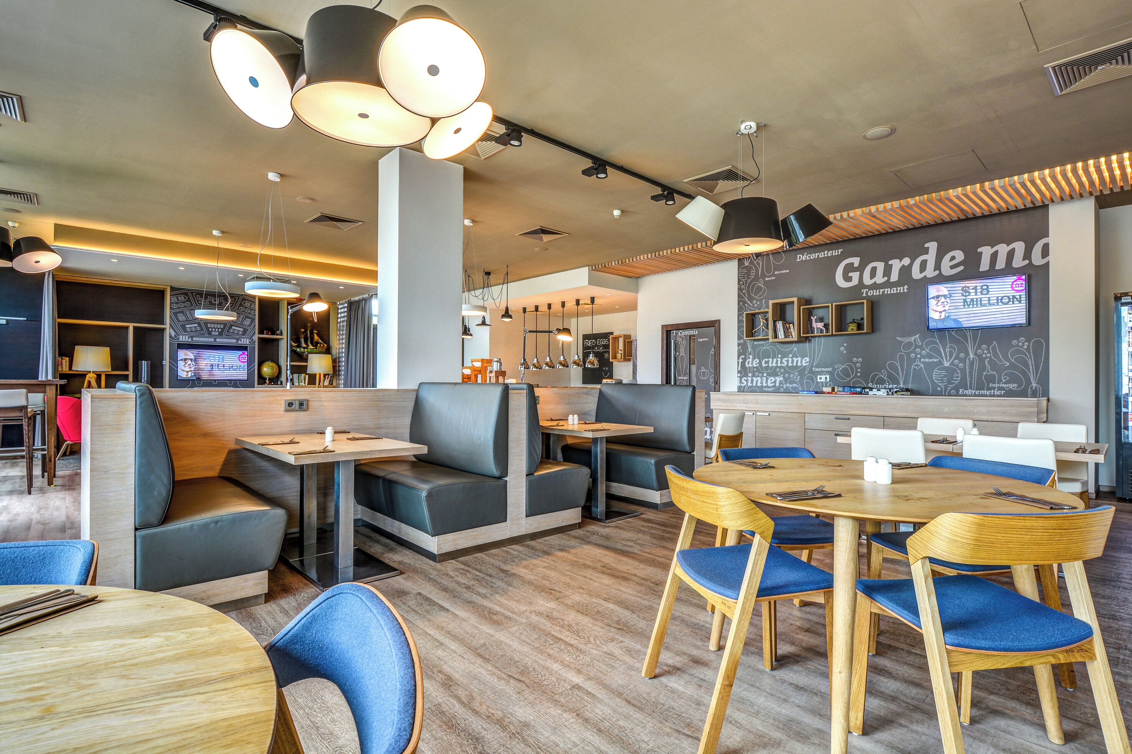 A modern restaurant interior with booths and tables, a chalkboard menu, and pendant lighting.
