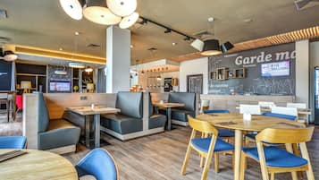 A modern restaurant interior with booths and tables, a chalkboard menu, and pendant lighting.