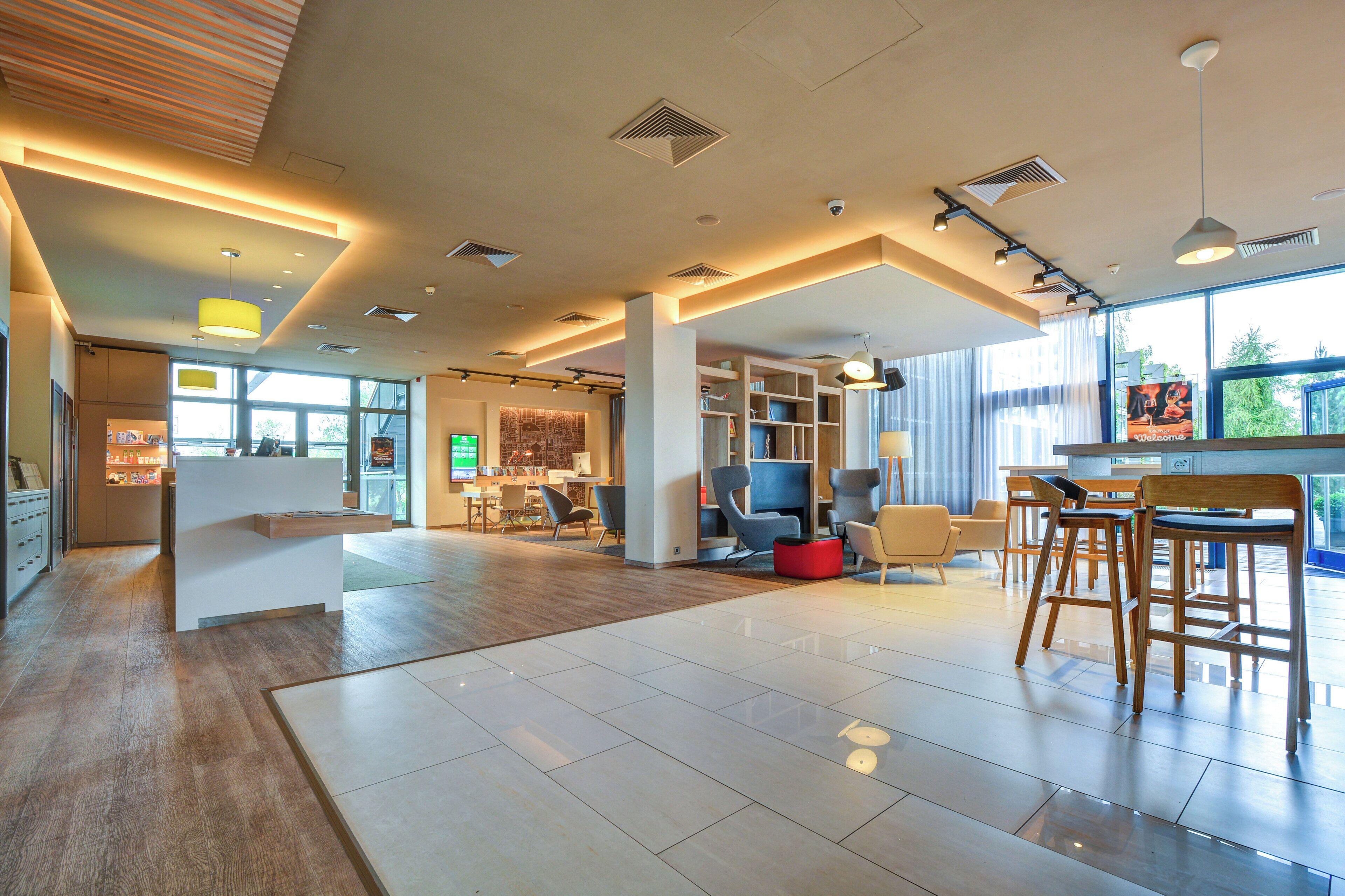 Eine geräumige Lobby mit einer Rezeption, einer Sitzecke und großen Fenstern, die natürliches Licht hereinlassen.